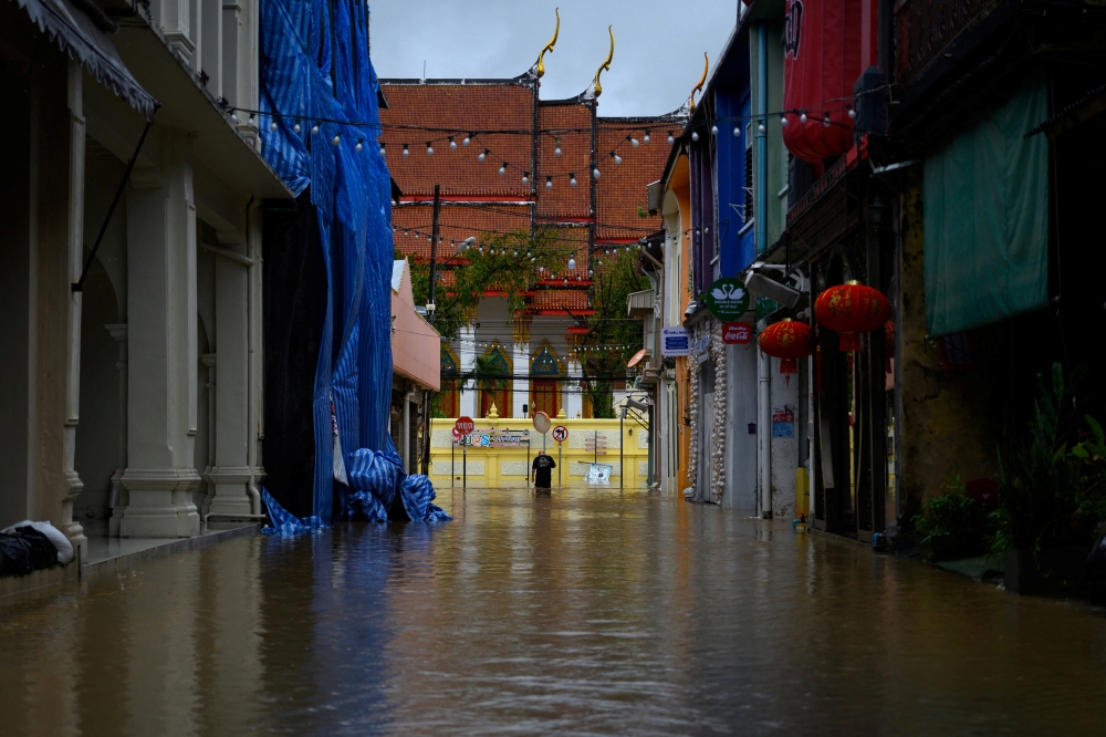 A man walks in a flooded street in the tourist area of Phuket Town in Phuket, Thailand October 16, 2022. REUTERS/Chanchai Hatsut