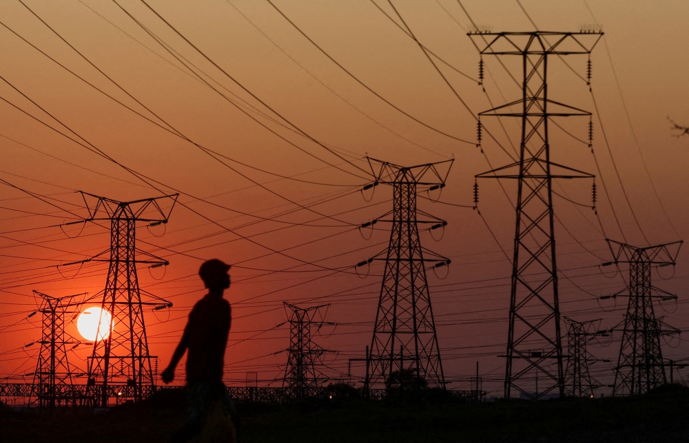 A local walks past electricity pylons during frequent power outages from South African utility Eskom, caused by its aging coal-fired plants, in Orlando, Soweto, South Africa, September 28, 2022. (REUTERS/Siphiwe Sibeko)
