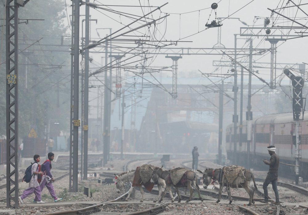 File Photo: School girls and mules are seen crossing railway tracks on a smoggy morning in New Delhi, India, December 2, 2021. (REUTERS/Anushree Fadnavis)