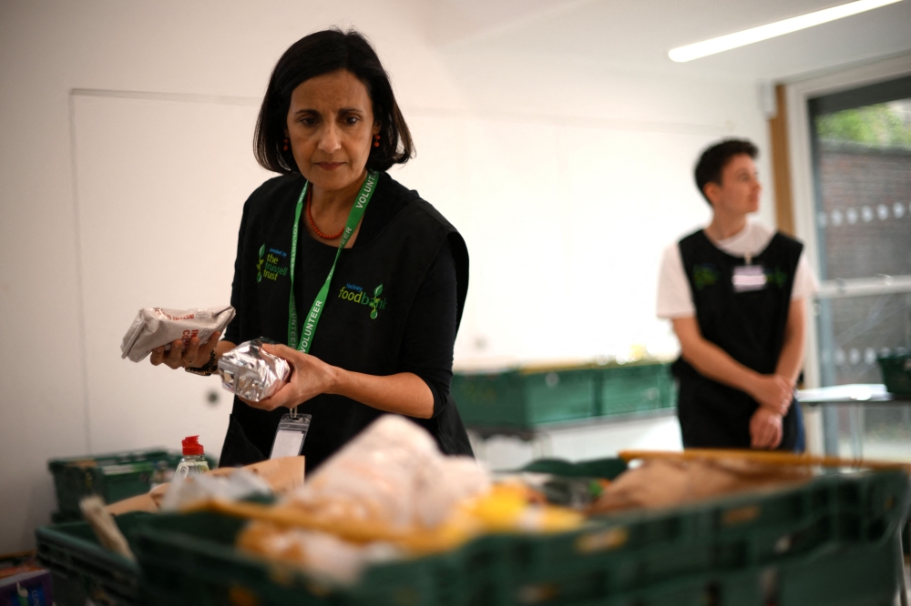 A member of staff sorts through food items inside a foodbank in Hackney, north-east London on October 31, 2022. There were dozens of people on Monday queuing outside the Foodbank in Hackney, an east London district, with a voucher allowing them to obtain a basket containing three days' worth of food. (Photo by Daniel LEAL / AFP)