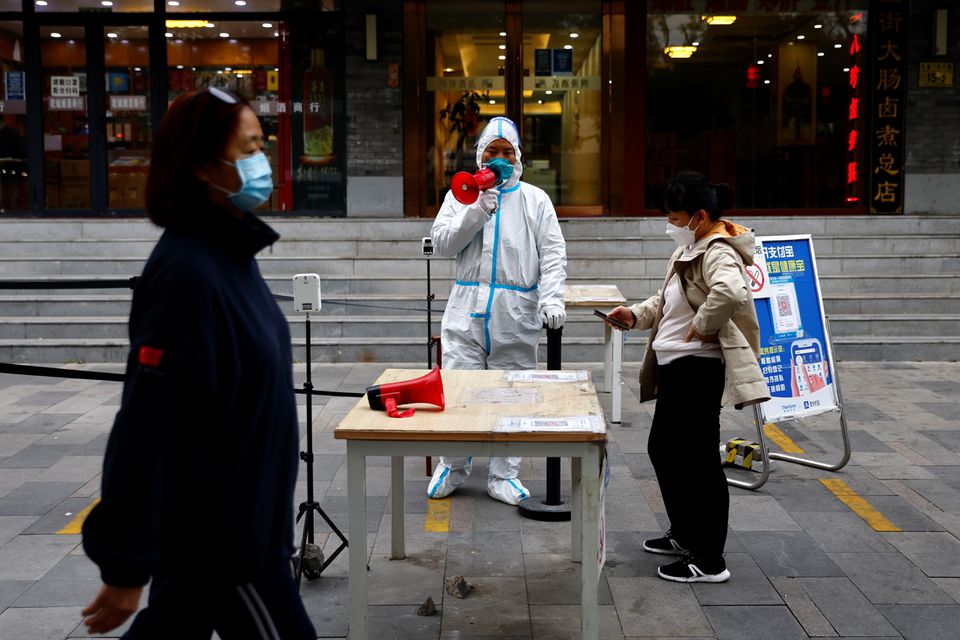 A worker in a protective suit guides people to scan QR health code before taking a test for the coronavirus disease (COVID-19) at a testing booth, in Beijing, China, on October 27, 2022. REUTERS/Tingshu Wang/File Photo