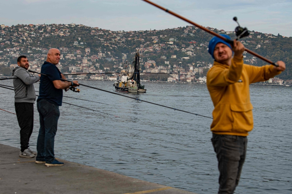 Anglers fish on the bank of the Bosphorus as a fishing boat lays its nets in the Marmara sea off the cost of Istanbul, on November 6, 2022. Photo by Yasin Akgul / AFP