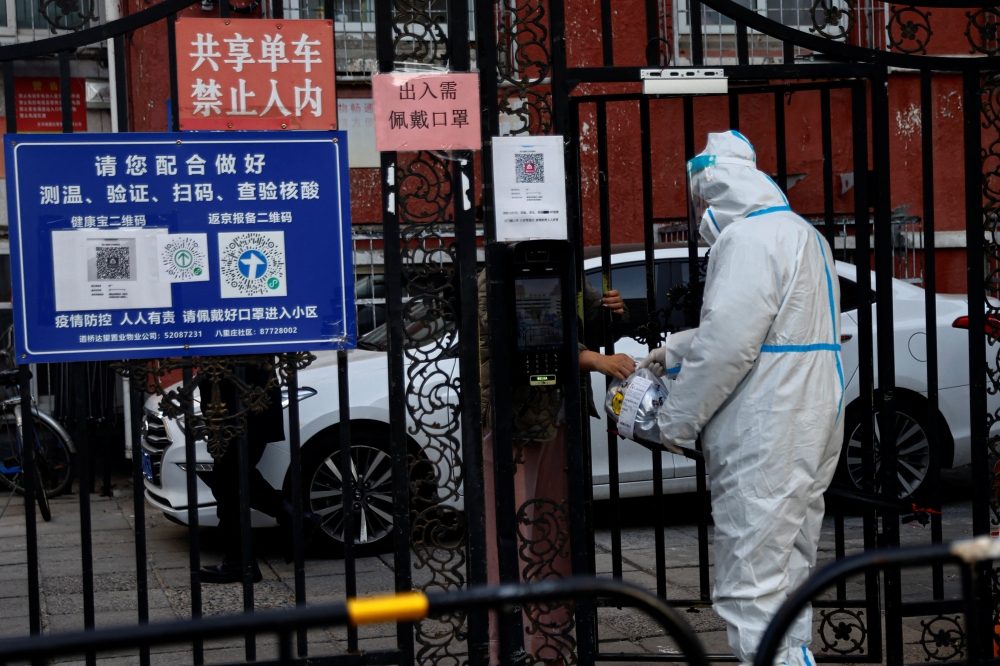 A worker in a protective suit passes a delivery good to a resident through a gate of a residential compound that is still under lockdown, following a coronavirus disease (COVID-19) outbreak, in Chaoyang District of Beijing, China, on November 26, 2022. REUTERS/Tingshu Wang