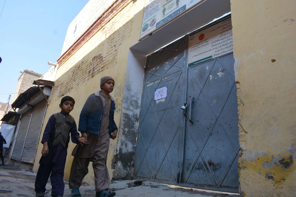 Children walk past a locked school gate after Taliban militants seized a police station in Bannu on December 20, 2022. (Photo by Karim ULLAH / AFP)
 