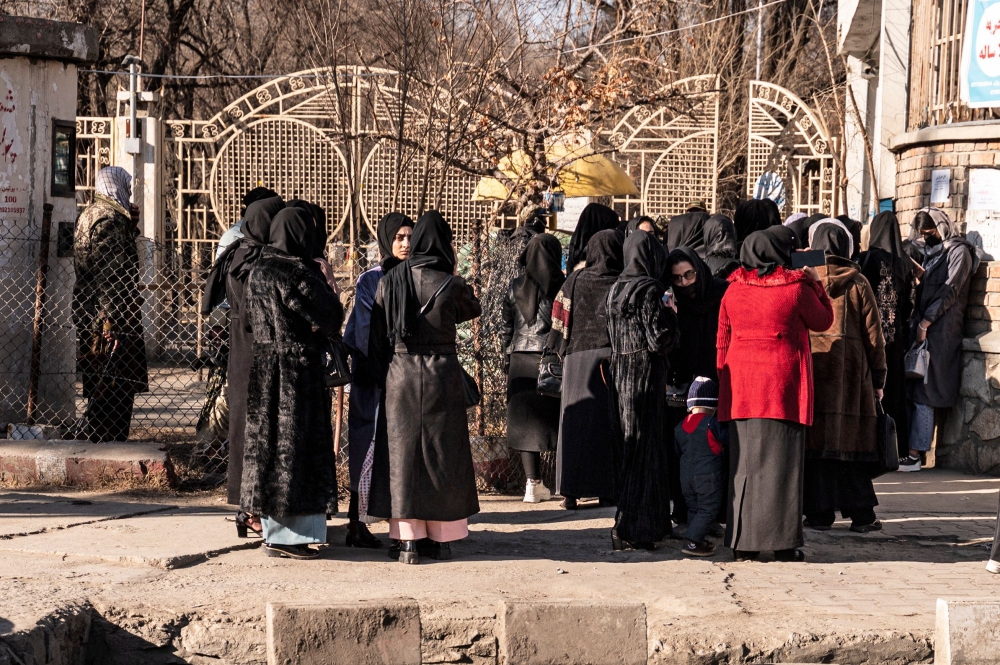 Afghan female university students stop by Taliban security personnel stand next to a university in Kabul on December 21, 2022. (Photo by Wakil Kohsar / AFP)