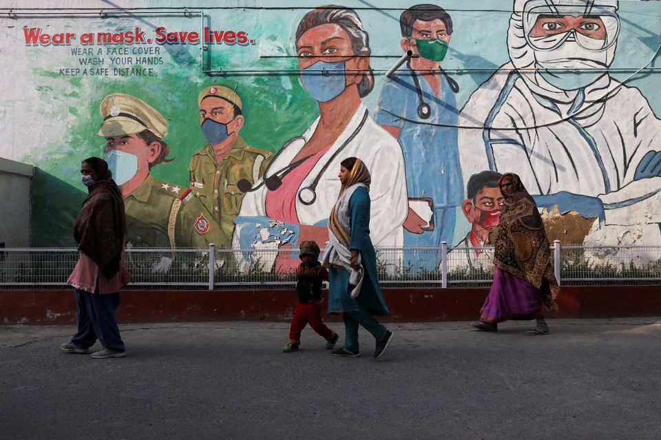 Women walk past a graffiti amidst the spread of the coronavirus disease (COVID-19) in New Delhi, India, February 7, 2022. REUTERS/Anushree Fadnavis
