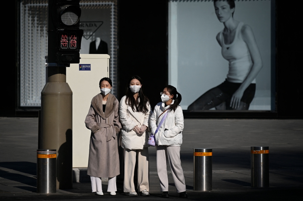 People wait to cross a street in Beijing on December 26, 2022. (Photo by Wang Zhao / AFP)