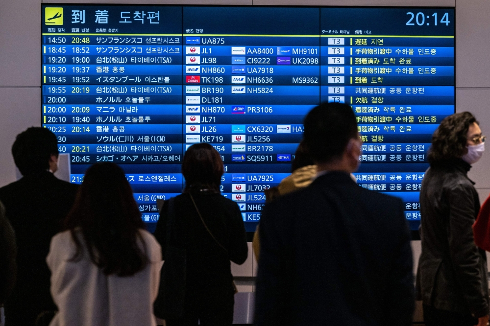 People wait in front a board showing international flight arrivals at Tokyo's Haneda international airport on December 28, 2022. Photo by Philip FONG / AFP