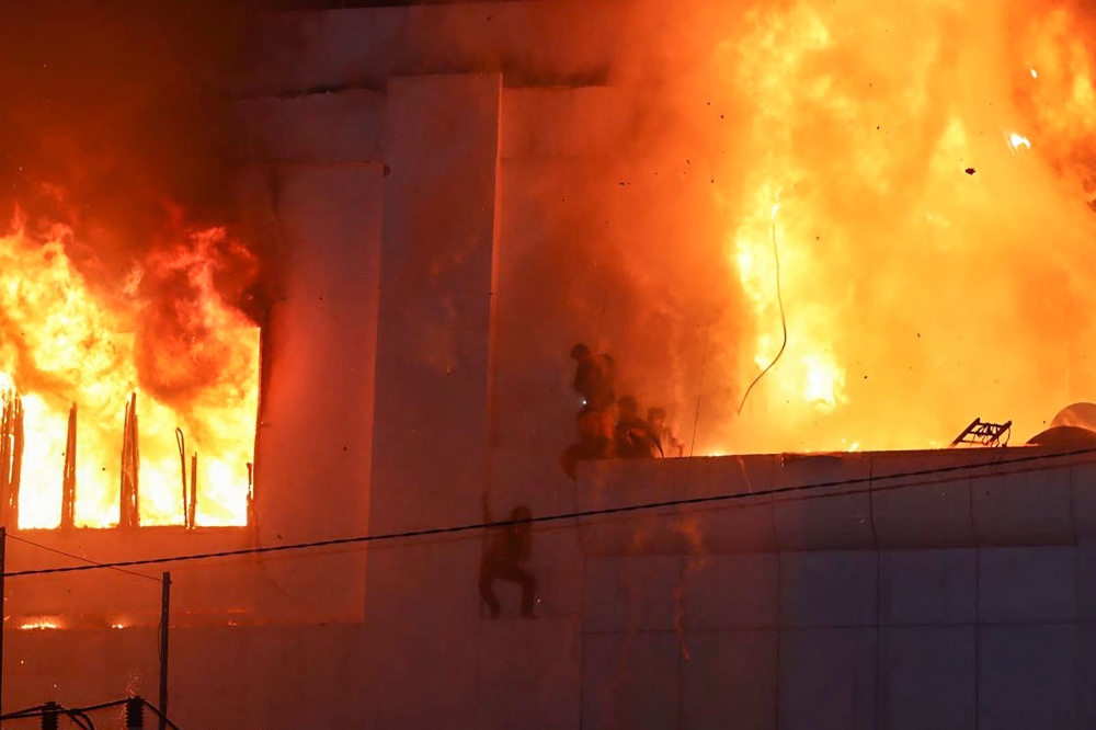 Fire burns around people on a ledge on the side of the Grand Diamond City hotel-casino in Poipet on December 29, 2022. (AFP)