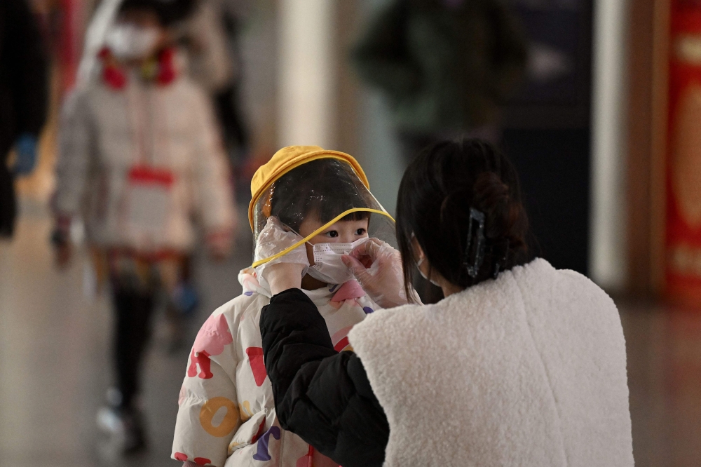 A woman arranges a face mask on a child's face in a departure terminal of the international airport in Beijing on December 29, 2022. (Photo by Noel Celis / AFP)