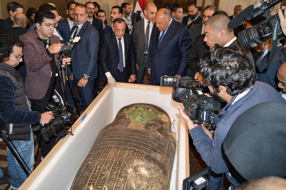 Egypt's Foreign Minister Sameh Shoukry (center right) and the head of the Supreme Council of Antiquities Mostafa Waziri (center left) are surrounded by journalists as they inspect an ancient Egyptian wooden sarcophagus being handed over and which was formerly displayed at Houston Museum of Natural Sciences after having been looted and smuggled years prior, at the foreign ministry headquarters in the capital Cairo on January 2, 2023. (Photo by AFP)