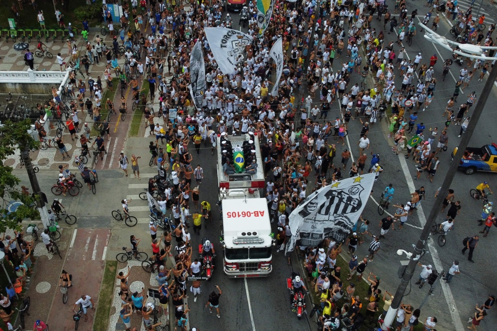 In this aerial picture fans of the late Brazilian football star Pele gather on the street as a firetruck transports Pele's coffin to the Santos' Memorial Cemetery in Santos, Sao Paulo state, Brazil on January 3, 2023.  (Photo by Miguel SCHINCARIOL / AFP)
 