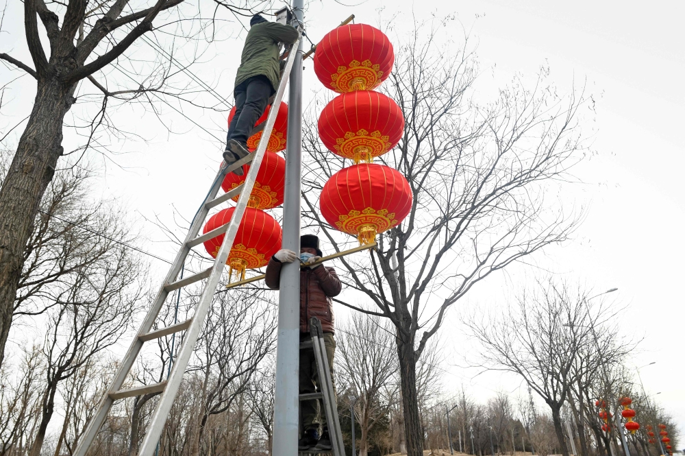 Workers hang red lanterns on a light pole along a street for the upcoming Chinese Lunar New Year celebrations in Beijing on January 14, 2023. (Photo by WANG Zhao / AFP)