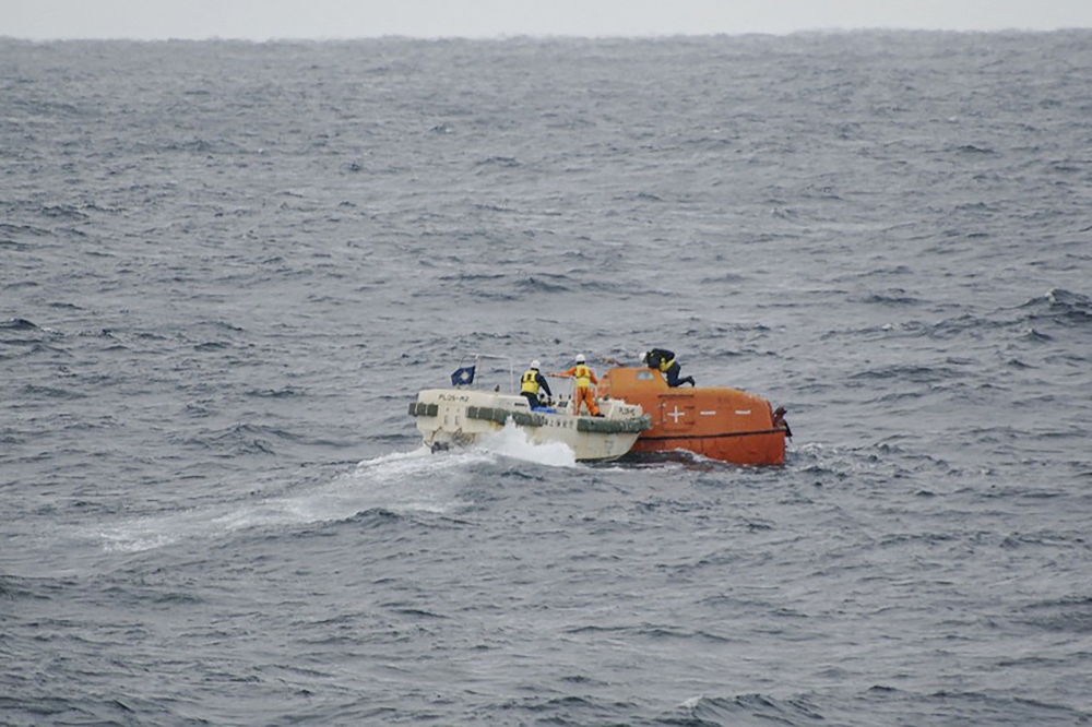 This handout photo taken and released on January 25, 2023 by the 7th Regional Coast Guard headquarters of the Japan Coast Guard shows Coast Guard personnel (centre L) checking on a lifeboat (centre R-in orange) from the Jin Tian cargo ship floating at sea. (Photo by Handout / Japan Coast Guard / AFP)