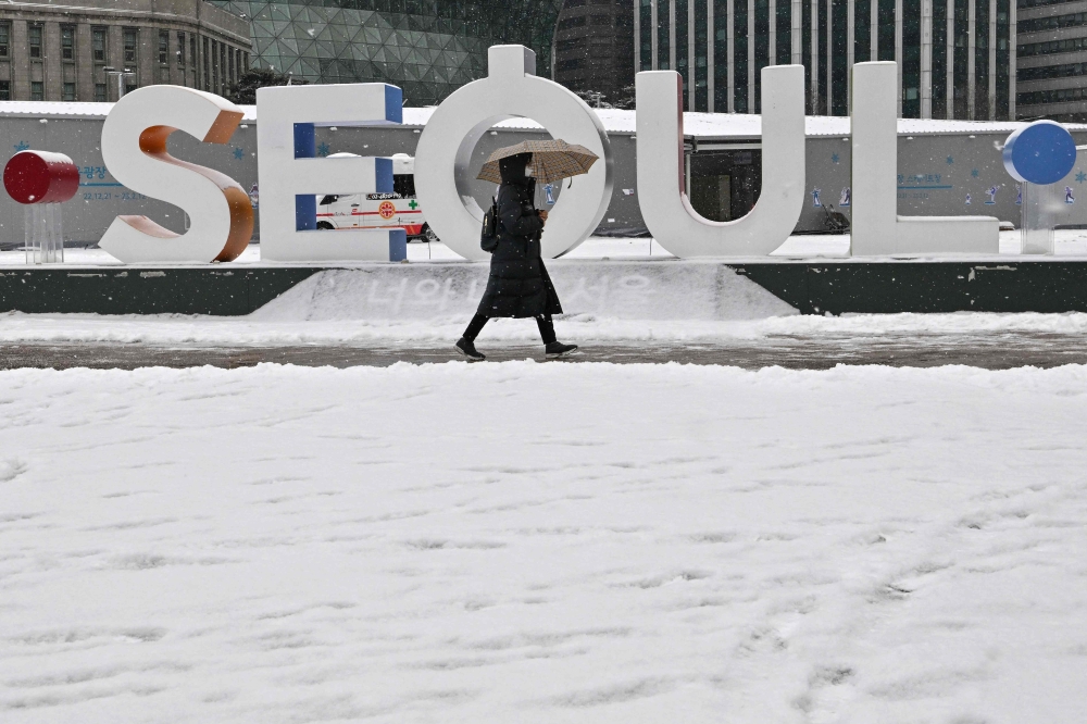 A woman walks along a snow-covered street in front of City Hall during snowfall in Seoul on January 26, 2023. (Photo by Jung Yeon-je / AFP)