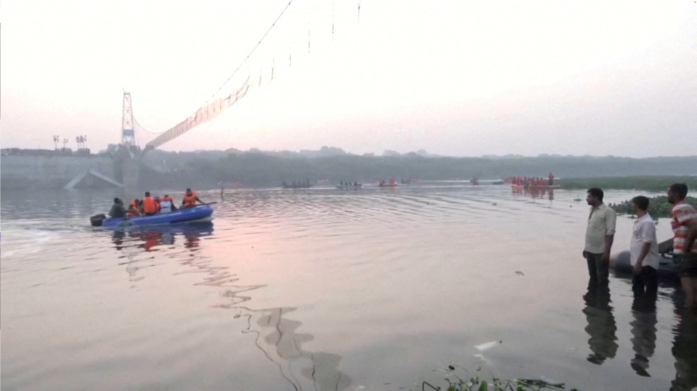 People look on as rescuers in boats work at the site of a suspension bridge collapse in Morbi town in the western state of Gujarat, India, October 31, 2022. ANI via REUTERS