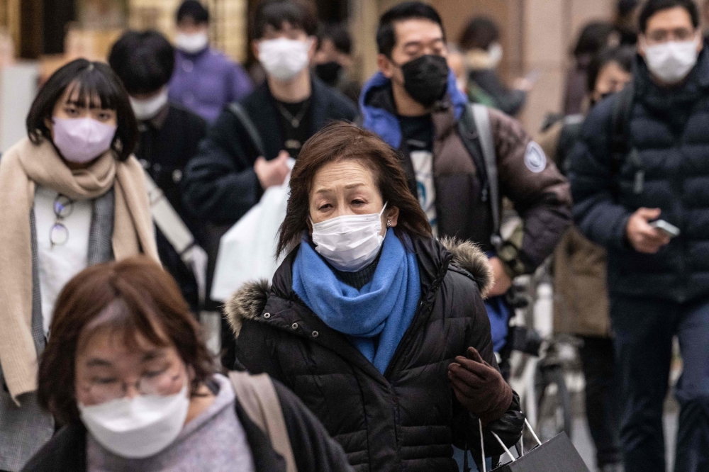 People wearing face masks cross a street in Tokyo on January 27, 2023. (Photo by Yuichi YAMAZAKI / AFP)