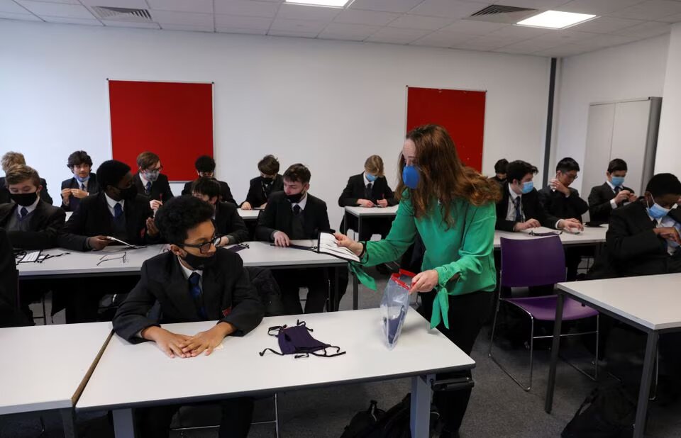 A teacher hands out face masks to students on the first day back at school, as the coronavirus disease (COVID-19) lockdown begins to ease, at Fulham Boys School in London, Britain, on March 8, 2021. File Photo / Reuters
