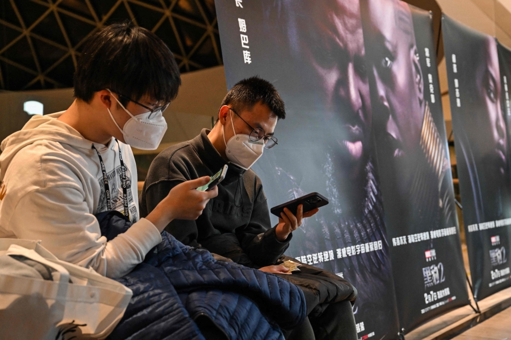 Two men look at their smartphone as they wait to watch the movie 
