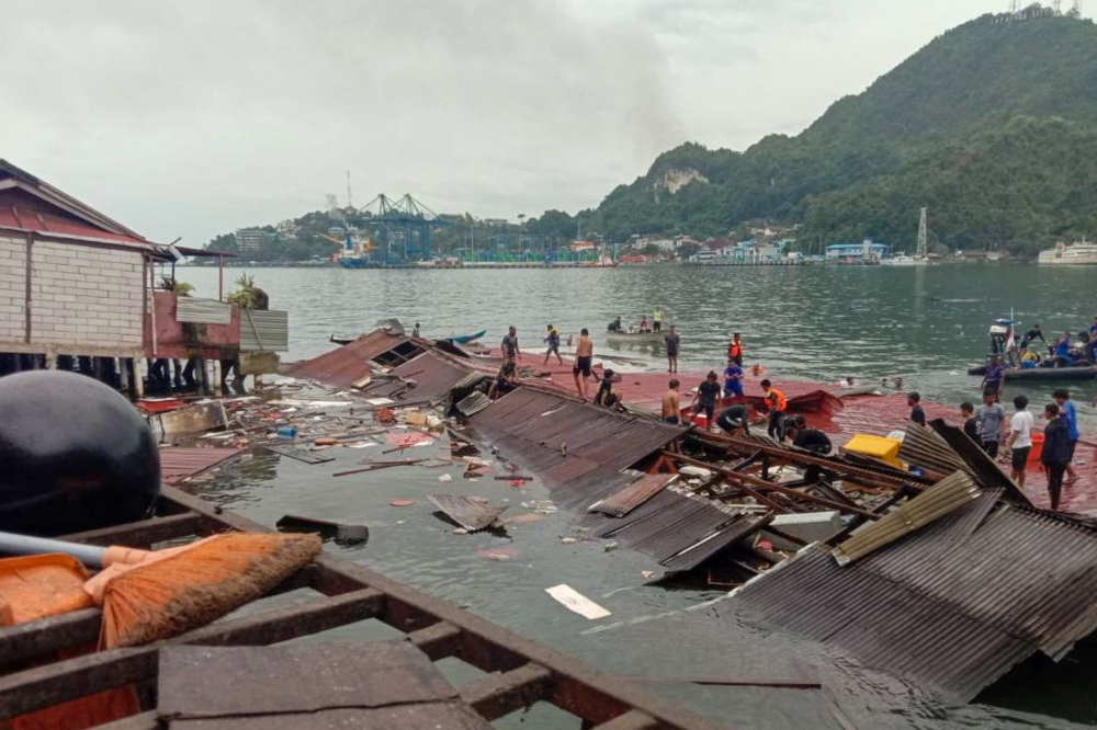 People stand on the roofing of collapsed shops in the port after a 5.1-magnitude earthquake in Jayapura, Indonesia's eastern province of Papua on February 9, 2023. (Photo by FAISAL NARWAWAN / AFP)