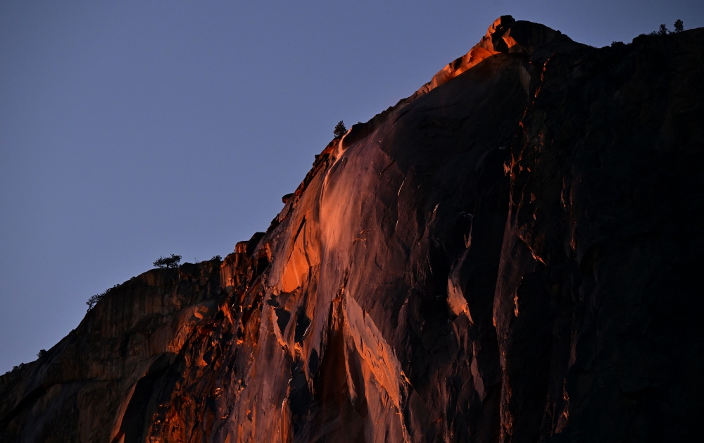 Water flowing off Horsetail Fall glows orange while backlit from the setting sun during the 