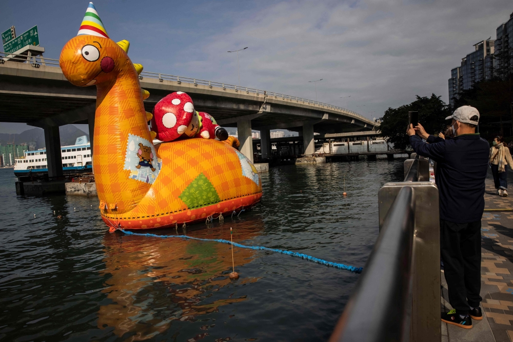 A man (R) takes a picture of a sculpture (L) floating on the water in the North Point district of Hong Kong on February 16, 2023. (Photo by ISAAC LAWRENCE / AFP)