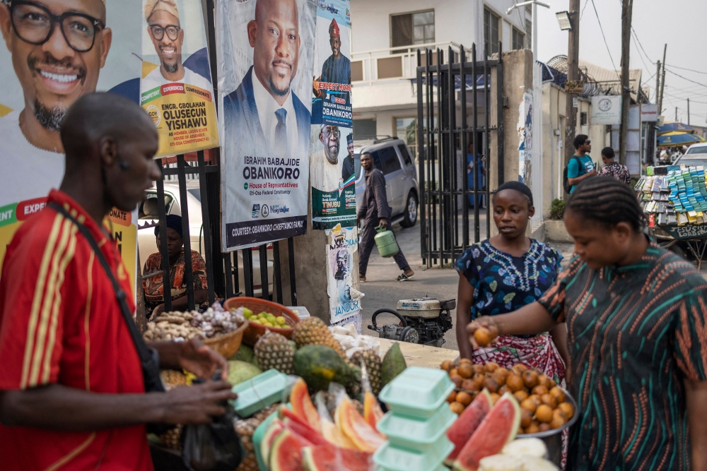 A woman buys fruits from a street vendor nexy to a campaign poster of presidential candidate of the ruling Action Progressives Congress (APC) Bola Ahmed Tinubu and running mate Kashim Shettima in a market in Lagos on February 16, 2023. (Photo by Michele Spatari / AFP)