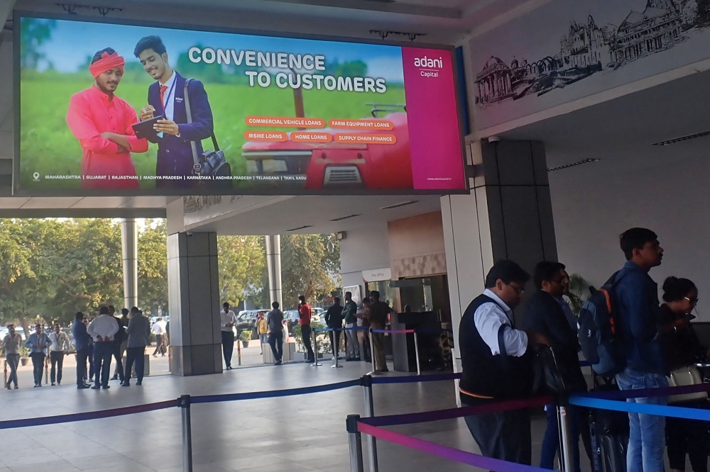 File photo: Travellers stand near a billboard of Adani Capital at Sardar Vallabhbhai Patel international airport in Ahmedabad on January 30, 2023. (Photo by Sam PANTHAKY / AFP)

