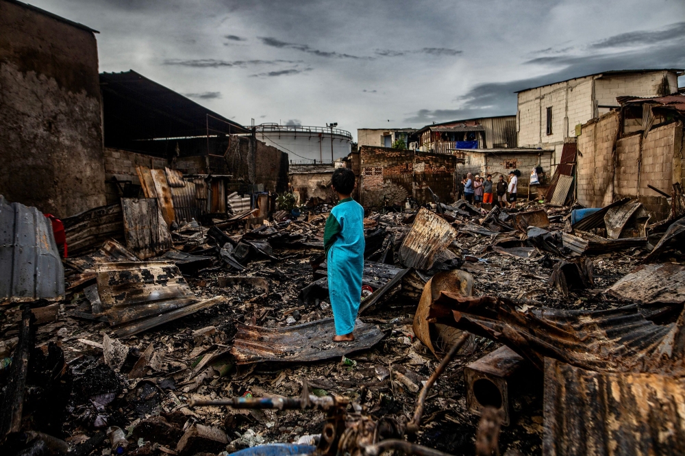 A boy stands in the remains of a burnt house in a residential area in Plumpang, north Jakarta on March 4, 2023, after a fire at a nearby state-run fuel storage depot run by energy firm Pertamina. (Photo by Aditya Aji / AFP)