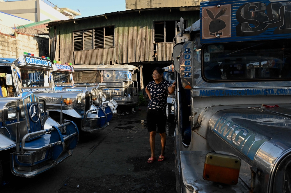 A woman stands beside a parked jeepneys in Quezon City on March 6, 2023. Photo by JAM STA ROSA / AFP