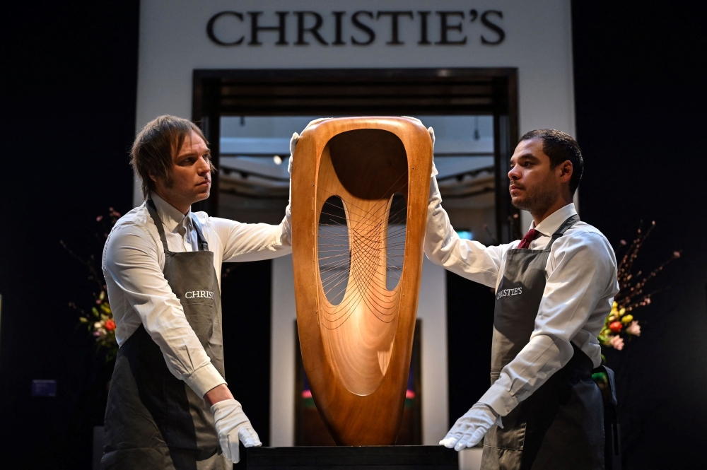 Two gallery assistants hold a sculpture by British artist Barbara Hepworth called 