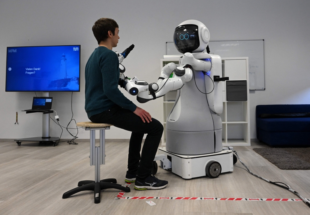 An employee sits in front of the robot Garmi in the laboratory of the Research Center Geriatronics of the Technical University Munich, in Garmisch-Partenkirchen, southern Germany, on March 6, 2023. (Photo by Christof Stache / AFP)