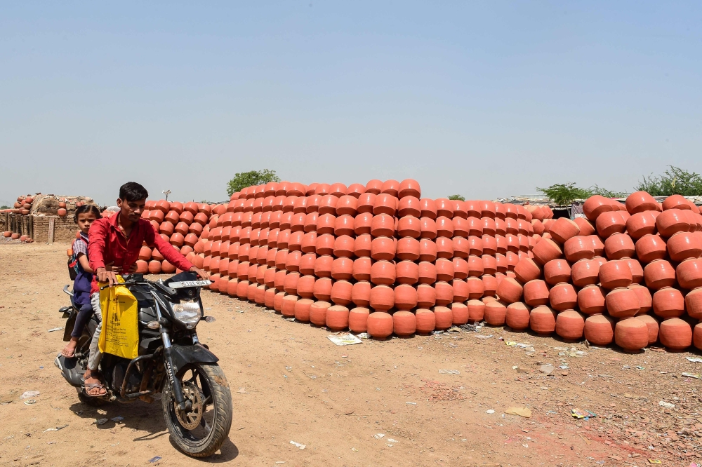 A motorist drives past a stack of clay pots which are popularly used to store drinking water during the summer season, at a village on the outskirts of Ahmedabad on March 27, 2023. (Photo by SAM PANTHAKY / AFP)

