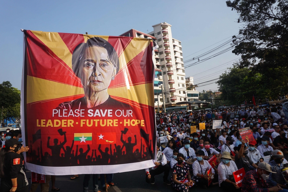 In this file photo taken on February 15, 2021 a banner featuring Aung San Suu Kyi is displayed as protesters take part in a demonstration against the military coup in front of the National League for Democracy (NLD) office in Yangon.  (Photo by AFP)