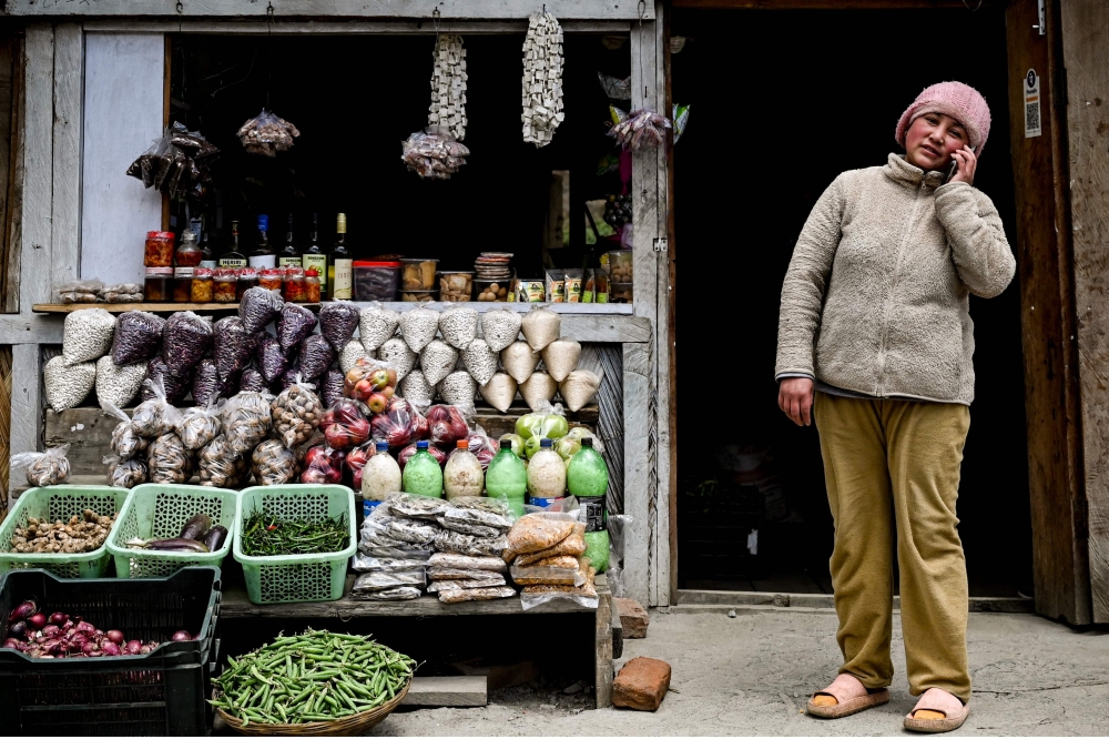 A shopkeeper speaks on her phone as she waits for customers at her shop along a road in India's north-eastern state, Arunachal Pradesh on April 2, 2023. (Photo by Arun Sankar / AFP)