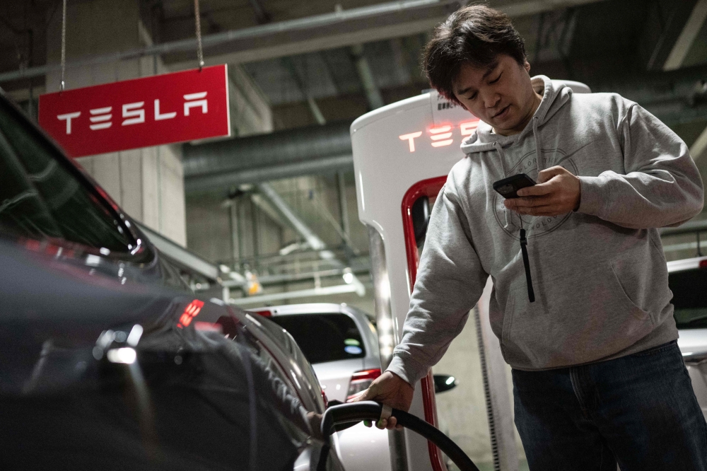 This photo taken on January 27, 2023 shows Atsushi Ikeda, the founder and vice president of a Japanese club for Tesla owners, checking his phone as he charges his Tesla Model S at a charging station in Tokyo. Photo by Yuichi YAMAZAKI / AFP
