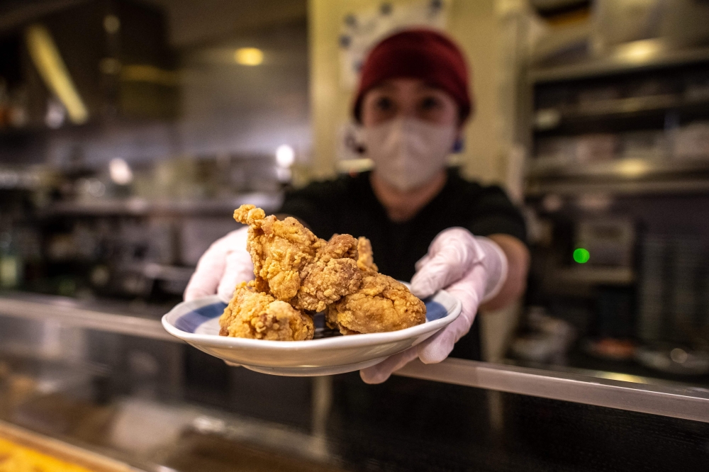 This picture taken on March 1, 2023 shows Hiromi Matsumoto serving a plate of karaage, a Japanese style fried chicken at an izakaya food store in Tokyo. Photos by Philip FONG / AFP