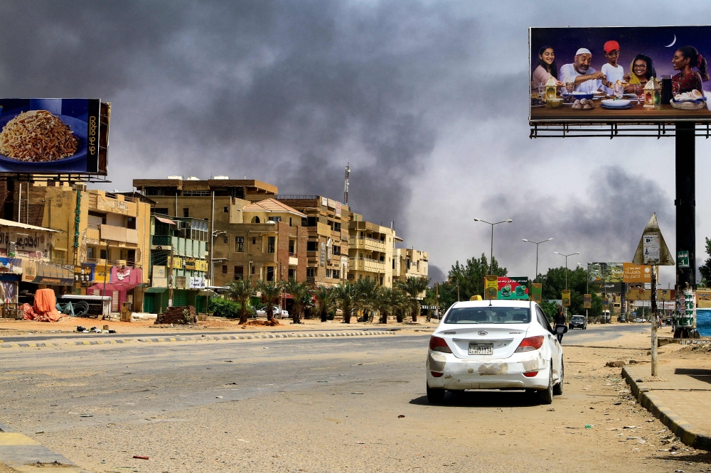 Smoke rises in the background as a car drives along an almost deserted street in Khartoum on April 16, 2023, during ongoing fighting between the forces of 2 rival generals. (Photo by AFP)