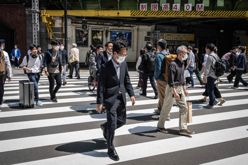 People cross a street in Yurakucho district of Tokyo on April 28, 2023. (Photo by Yuichi Yamazaki / AFP)