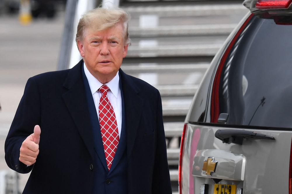 Former US President Donald Trump gestures to members of the media on the tarmac after disembarking 