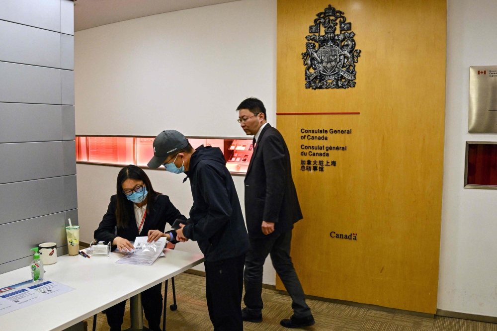 A worker (L) at the Consulate General of Canada tends to a man at the entrance of the consulate in Shanghai on May 9, 2023. (Photo by Hector Retamal / AFP)