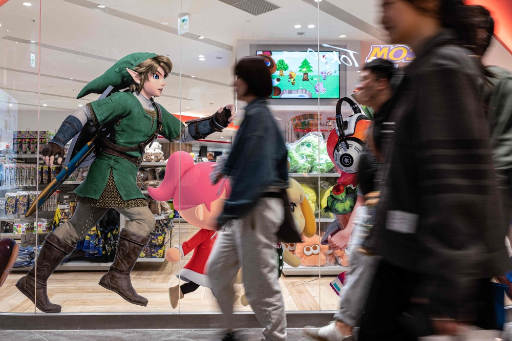 This photo taken on May 8, 2023 shows people walking past an illustration (L) for Japanese gaming giant Nintendo's long-running 