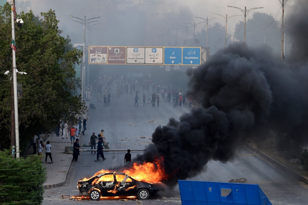 A car is seen burning along a road as Pakistan Tehreek-e-Insaf (PTI) party activists and supporters of former Pakistan's Prime Minister Imran block a road during a protest against the arrest of their leader in Karachi on May 9, 2023. (Photo by Asif Hassan / AFP)