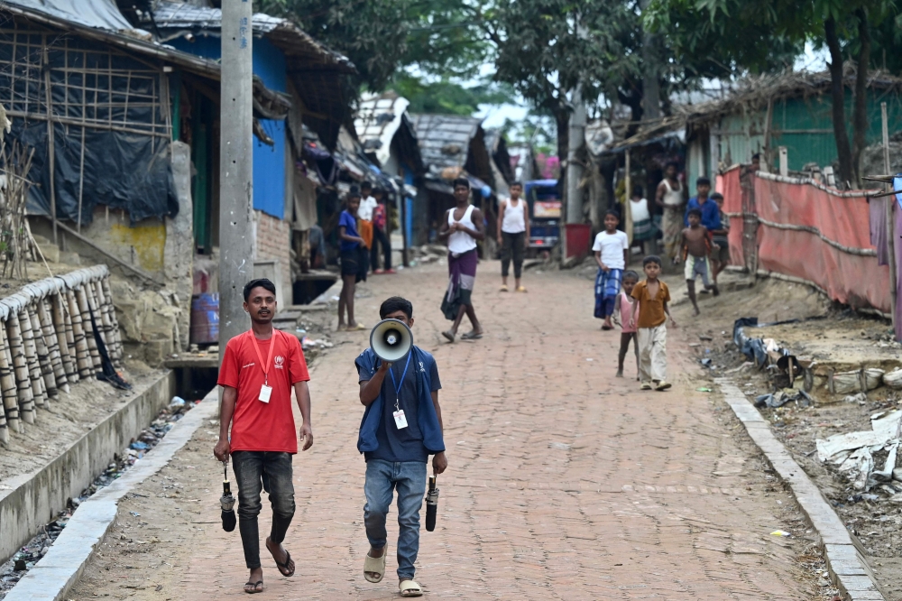 United Nations High Commissioner for Refugees workers use a megaphone to alert the public ahead of Cyclone Mocha landfall, at Nayapara Rohingya refugee camp in Teknaf on May 13, 2023. (Photo by Munir uz zaman / AFP)