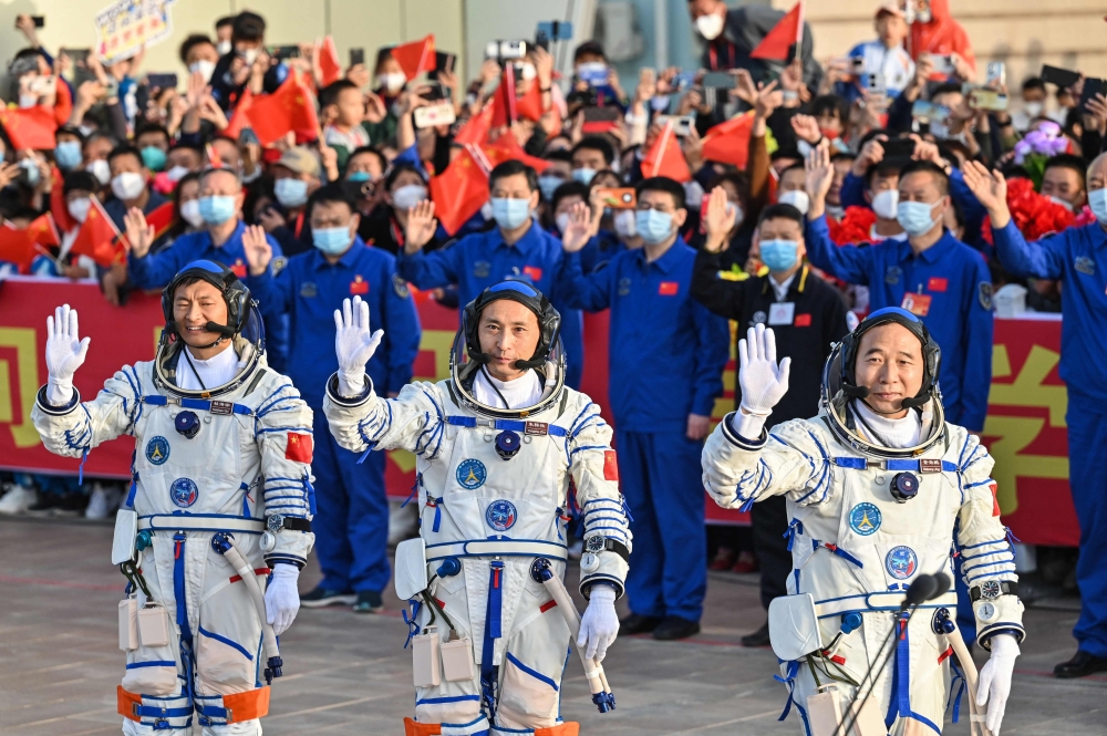 Gui Haichao (L) payload expert, Zhu Yangzhu (C) space flight engineer and commander Jing Haipeng (R) wave during the seeing-off ceremony on May 30, 2023. (Photo by Hector Retamal / AFP)