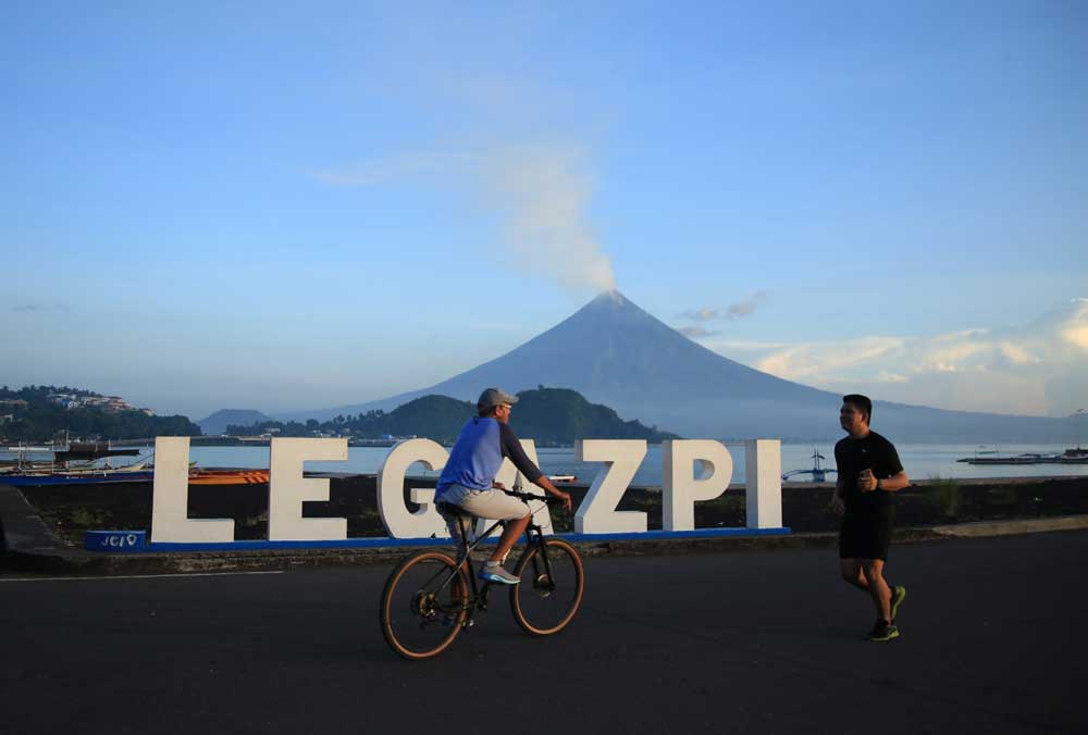 Residents exercise as Mayon volcano spews white smoke in Legaspi City, Albay province on June 7, 2023. (Photo by Charism SAYAT / AFP)
