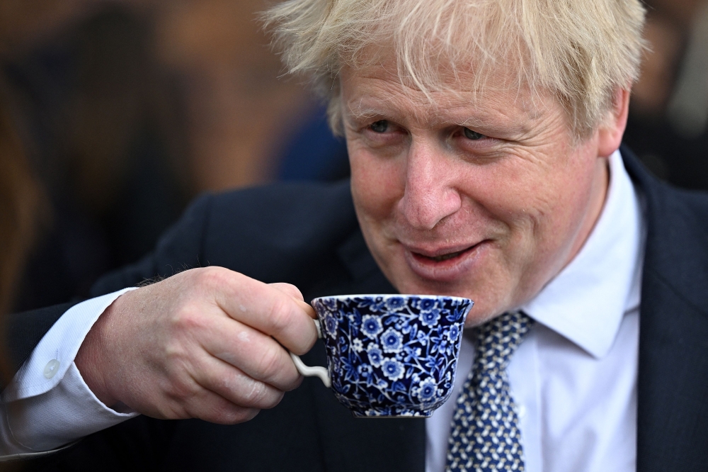 (FILES) In this file photo taken on May 12, 2022 Britain's then prime minister Boris Johnson drinks from a cup as he talks with local business leaders after hosting a cabinet away day in Stoke-on-Trent, central England, on May 12, 2022. (Photo by Oli SCARFF / POOL / AFP)
