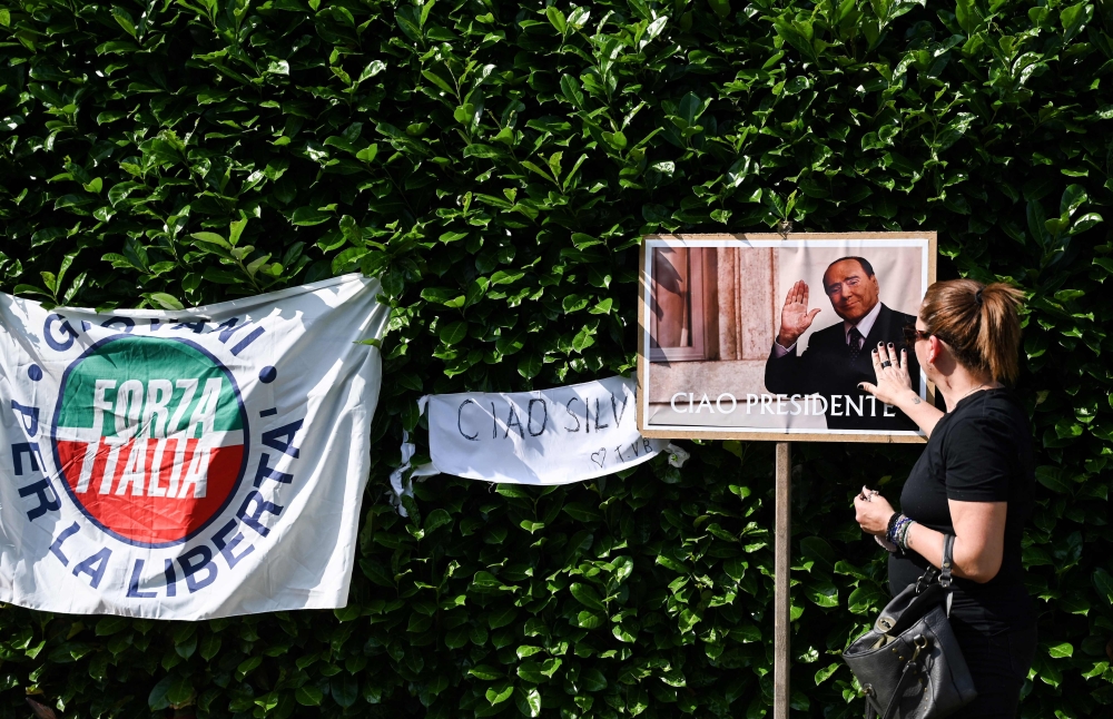 A mourner touches a picture of Italian businessman and former prime minister Silvio Berlusconi, during a tribute following his death, outside of his residence Villa San Martino, in Arcore, northern Italy, on June 12, 2023. (Photo by GABRIEL BOUYS / AFP)
