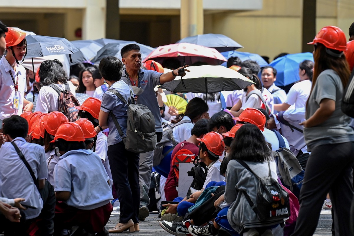 A school staff member instruct students as they evacuate a building in Manila on June 15, 2023, following a magnitude 6.2 earthquake struck the Philippines. (Photo by JAM STA ROSA / AFP)