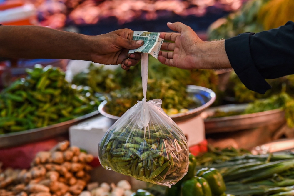 A customer buys vegetables from a stall at a market in Karachi on July 3, 2023. (Photo by Asif HASSAN / AFP)
